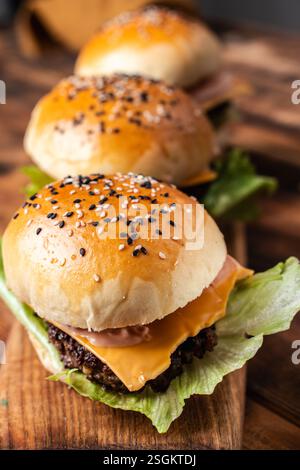 Drei Burger mit Patty, Käse und Salat auf Holzbrett und Hintergrund. Nahaufnahme. Hochwertige Fotos Stockfoto