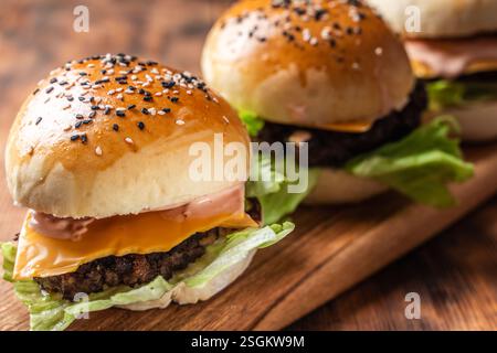 Drei Burger mit Patty, Käse und Salat auf Holzbrett und Hintergrund. Nahaufnahme. Leerzeichen für Text. Hochwertige Fotos Stockfoto