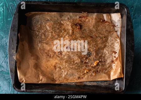 Backblech mit gebrauchtem Backpapier. Die Textur von schmutzigem Pergament auf dunkelgrünem Hintergrund. Hochwertige Fotos Stockfoto