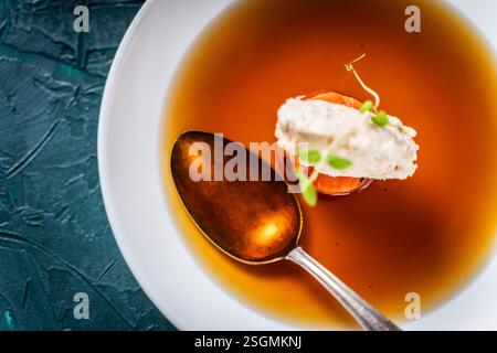 Suppe oder Consomme, dicke Fleischbrühe mit Karotten, Hühnerknödel serviert auf einem weißen Teller auf dunkelgrünem Hintergrund mit Löffel. Blick von oben. Spa Stockfoto