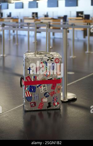 Koffer mit Reiseaufklebern im leeren Flughafenterminal mit Check-in-Schaltern im Hintergrund Stockfoto