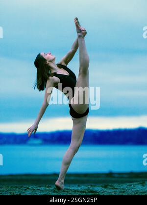 Eine Frau im schwarzen Trikot spielt Ballettpose an einem Strand mit ruhiger Wasserkulisse, USA Stockfoto