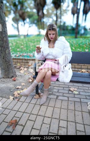 Junge Frau, die im Herbst Tablette benutzt und Kaffee im Park trinkt Stockfoto