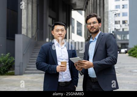 Porträt von zwei Geschäftsleuten in der Mittagspause. Kollegen, die vor dem Bürogebäude stehen und in Geschäftsanzügen gekleidet in die Kamera schauen. Stockfoto