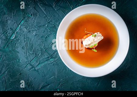 Suppe oder Consomme, dicke Fleischbrühe mit Karotten, Hühnerknödel und Mikrogrün, serviert auf einem weißen Teller auf dunkelgrünem Hintergrund. Blick aus der ganzen Welt Stockfoto