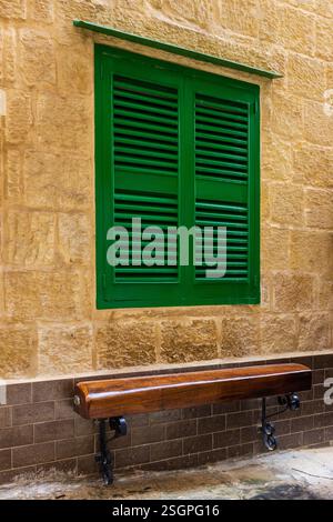 Grüne Holzläden und Bank auf rustikaler Steinmauer Stockfoto