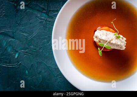 Suppe oder Consomme, dicke Fleischbrühe mit Karotten, Hühnerknödel und Mikrogrün, serviert auf einem weißen Teller auf dunkelgrünem Hintergrund. Blick aus der ganzen Welt Stockfoto