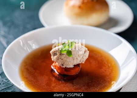 Suppe oder Consomme, dicke Fleischbrühe mit Karotten, Hühnerknödel serviert auf einem weißen Teller auf dunkelgrünem Hintergrund mit Sesambrötchen. Hohe Qual Stockfoto