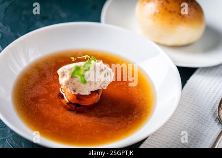 Suppe oder Consomme, dicke Fleischbrühe mit Karotten, Hühnerknödel serviert auf einem weißen Teller auf dunkelgrünem Hintergrund mit Sesambrötchen. Hohe Qual Stockfoto
