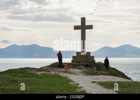 Ein Paar neben dem Steinkreuz an der Spitze von Ynys Llanddwyn und der Insel vor Anglesey an der Küste von Nordwales. Stockfoto