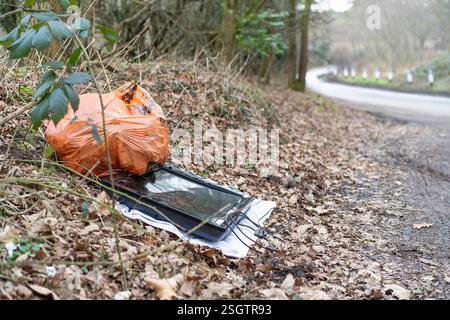 UK Fly Tipping: Eine Tüte mit Hausmüll und kaputtem Flachbildfernseher wurde auf einem Handtuch auf der Straße neben einer Landstraße (öffentliche Autobahn) abgelegt. Stockfoto