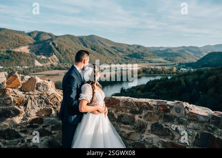 Das junge Brautpaar umarmt sich, steht am Aussichtspunkt und sieht die Landschaft herum. Stockfoto