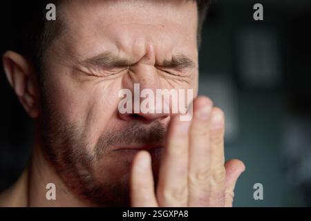 Schlechter Atem aus dem Mund. Nahaufnahme eines Mannes, der seinen Atem überprüft, indem er in seine Hand ausatmet, und zeigt Bedenken über Mundhygiene oder schlechten Atem Stockfoto