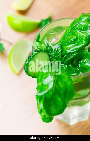 Erfrischendes grünes Getränk mit Basilikum und Gurke auf einer Holzoberfläche, umgeben von Limettenscheiben Stockfoto