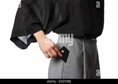 Kaukasische weibliche Hand, die schwarze Premium-Kreditkarte in graue Hosentasche auf weißem Hintergrund setzt. Geldfinanzierung Stockfoto