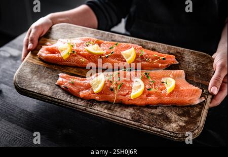 Mädchenhände halten frisches Forellenlachsfilet mit Kräutern und Zitronen. Frau kocht Omega-Orangenfisch mit Rosmarin für eine gesunde Ernährung Stockfoto