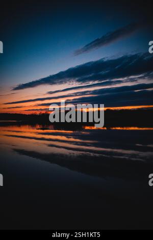 Dämmerungsreflektionen am Wasserrand – atemberaubende Sonnenuntergangstöne über ruhigen Gewässern Stockfoto