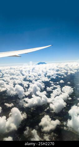 Blick vom Flugzeugfenster mit Mountain Peak über Wolken Stockfoto