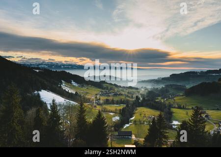 Die Sonne untergeht hinter der majestätischen Bergkette, goldene Strahlen durchdringen die Schichten der Wolken und werfen ein warmes Leuchten über das Tal Stockfoto