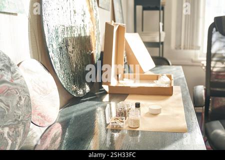 Kunststudio-Arbeitsbereich mit Gemälden, Kartons und Kunstgegenständen auf einem sonnigen Tisch. Stockfoto