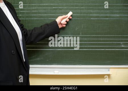 Die Hand eines selbstbewussten Lehrers hält ein Stück Kreide, bereit, während eines Unterrichts im Klassenzimmer auf die Tafel zu schreiben. Stockfoto