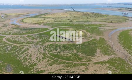 Aus der Vogelperspektive auf ein Küstenmoor mit grüner Vegetation, gewundenen Wasserkanälen und Wattenmeer. Die Landschaft zeigt Gezeitenmuster und ein Wrack W Stockfoto