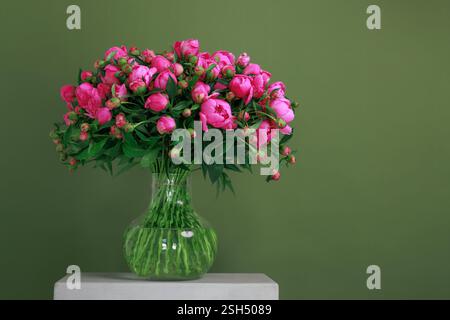 Üppige rosa Pfingstrosen in einer Glasvase vor einem eleganten grünen Hintergrund frisches, lebendiges und zeitloses Blumendekor perfekt für Innenarchitektur, Hochzeiten, Stockfoto