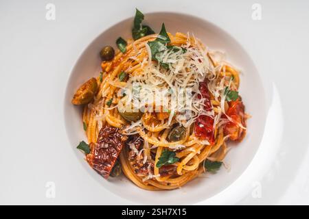 Spaghetti oder Puttanesca-Pasta nach traditionellem italienischem Rezept mit Sardellen, Oliven, Kapern und Tomaten auf einem weißen Teller. Nahaufnahme. Leerraum Stockfoto