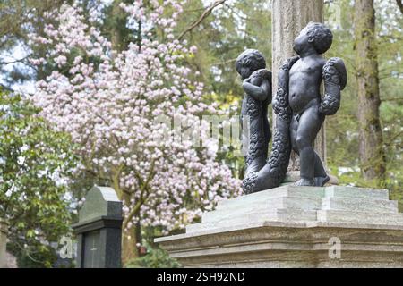 2 Kinderfiguren auf einem Grab, im Hintergrund ein Magnolienbaum (Magnilia) in Blüte, Waldfriedhof Dresden, Sachsen, Deutschland, Europa Stockfoto