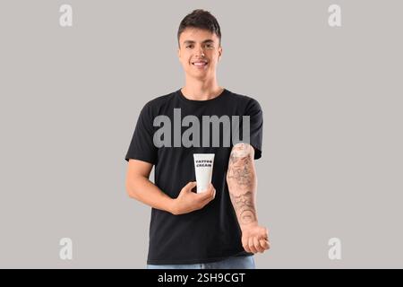 Junger Mann mit tätowiertem Arm und Tube Creme auf hellem Hintergrund Stockfoto