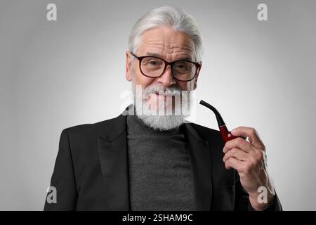 Seniorenmann mit Tabakpfeife auf hellgrauem Hintergrund Stockfoto