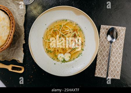 Klare Brühe mit Nudeln, Pilzen, Wachteleiern und Kräutern, serviert in einer Gourmet-Präsentation Stockfoto