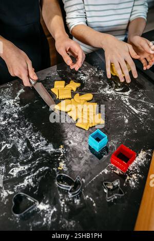 Nicht erkennbare Kinder, die Kekse mit verschiedenen Formen auf einer unordentlichen Küchentheke machen Stockfoto