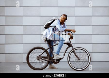 Attraktive schwarze Kerl Fahrrad fahren und Musik hören in der Nähe Backsteinmauer im Freien Stockfoto