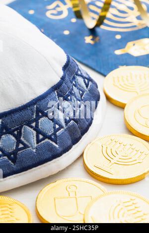 Eine weiße und blaue Garnmulke mit Goldmünzen und Serviette für die Hanukkah-Feier auf weißem Holzhintergrund Stockfoto