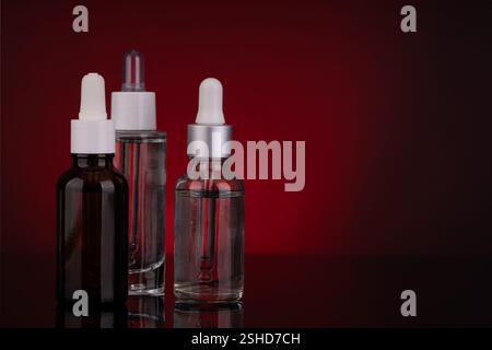 Drei Tropfflaschen aus Glas mit verschiedenen Designs auf rotem Hintergrund Stockfoto
