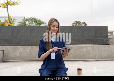 Junge weibliche medizinische Fachkraft, die ein Tablet im Freien verwendet, eine Pause genießen und die Patientenversorgung verbessern Stockfoto