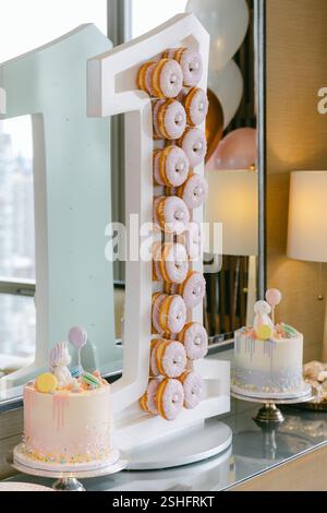 Ein festliches Geburtstagsfest mit einer riesigen Nummer Eins, Donuts und Pastell-Kuchen. Stockfoto