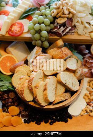 Eine Auswahl an Käse, Wurstwaren, frischem Obst und Brotscheiben sind wunderschön auf einer rustikalen Holzplatte angeordnet. Stockfoto