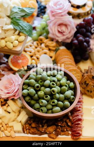 Eine wunderschön gestaltete Käse- und Wurstplatte umfasst Oliven, Früchte, Nüsse und Blumen für ein festliches Treffen. Stockfoto