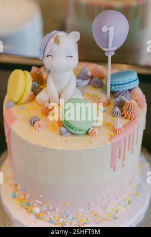 Ein lebendiger Kuchen mit Einhorndeckel, Macarons und Streuseln ist perfekt für einen festlichen ersten Geburtstag! Stockfoto