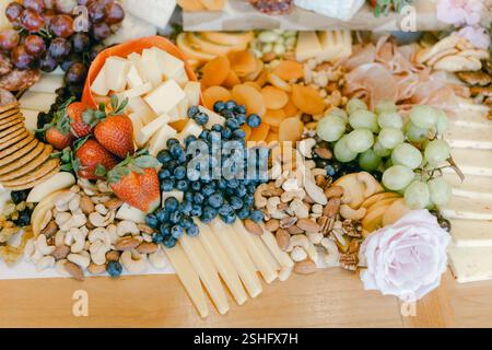 Eine lebhafte Auswahl an Früchten, Käse und Nüssen, die wunderschön auf einem Holztisch angeordnet sind, perfekt für Unterhaltung. Stockfoto