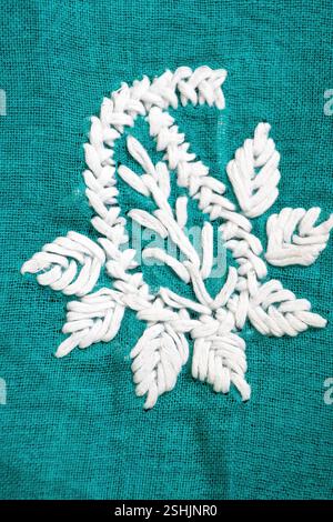 Eine Nahaufnahme aus filigranen, mit weißen Fäden aufgestickten Blüten, die blau-grüne Baumwolltextur zieren. Stockfoto