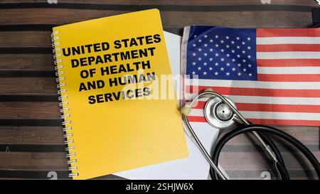 Konzept des United States Department of Health and Human Services Schreiben auf Buch und Flagge der Vereinigten Staaten isoliert auf Holztisch. Stockfoto