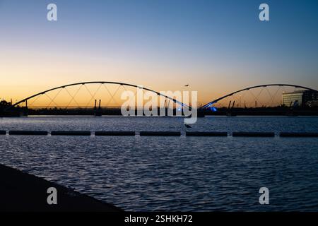 Die atemberaubende Fußgängerbrücke Tempe Town Lake steht hoch vor der Kulisse eines farbenfrohen Sonnenuntergangs, deren elegantes architektonisches Design sich in der widerspiegelt Stockfoto