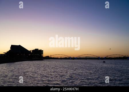 Ein ruhiger Abendblick auf den Tempe Town Lake, mit den goldenen Tönen der untergehenden Sonne, die ein friedliches Leuchten über dem Wasser ausstrahlt. Die Silhouette des Buildi Stockfoto