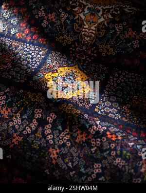 Nahtdetails eines aufwändig gemusterten Teppichs in Dunkelblau und Gold mit persischem Blumenmuster in sanftem Licht Stockfoto
