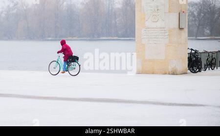 Hannover, Deutschland. Februar 2025. Eine Frau fährt mit dem Fahrrad über das schneebedeckte Nordufer des Maschsees. Quelle: Julian Stratenschulte/dpa/Alamy Live News Stockfoto