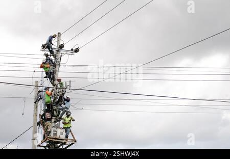 Arbeiter, die elektrische Instandhaltung an Stromleitungen in Indonesien durchführen und Teamarbeit und Sicherheitspraktiken bei bewölktem Himmel vorführen Stockfoto