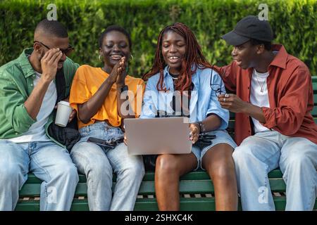 Multikulturelle Gruppe von Freunden, die sich Filme auf einem Laptop im Park ansehen, entspannen und das Wochenende im Freien genießen Stockfoto
